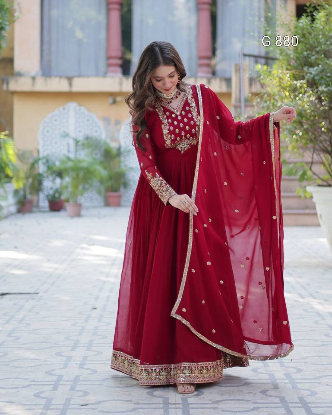 Woman in a red traditional outfit with gold embroidery standing outdoors.