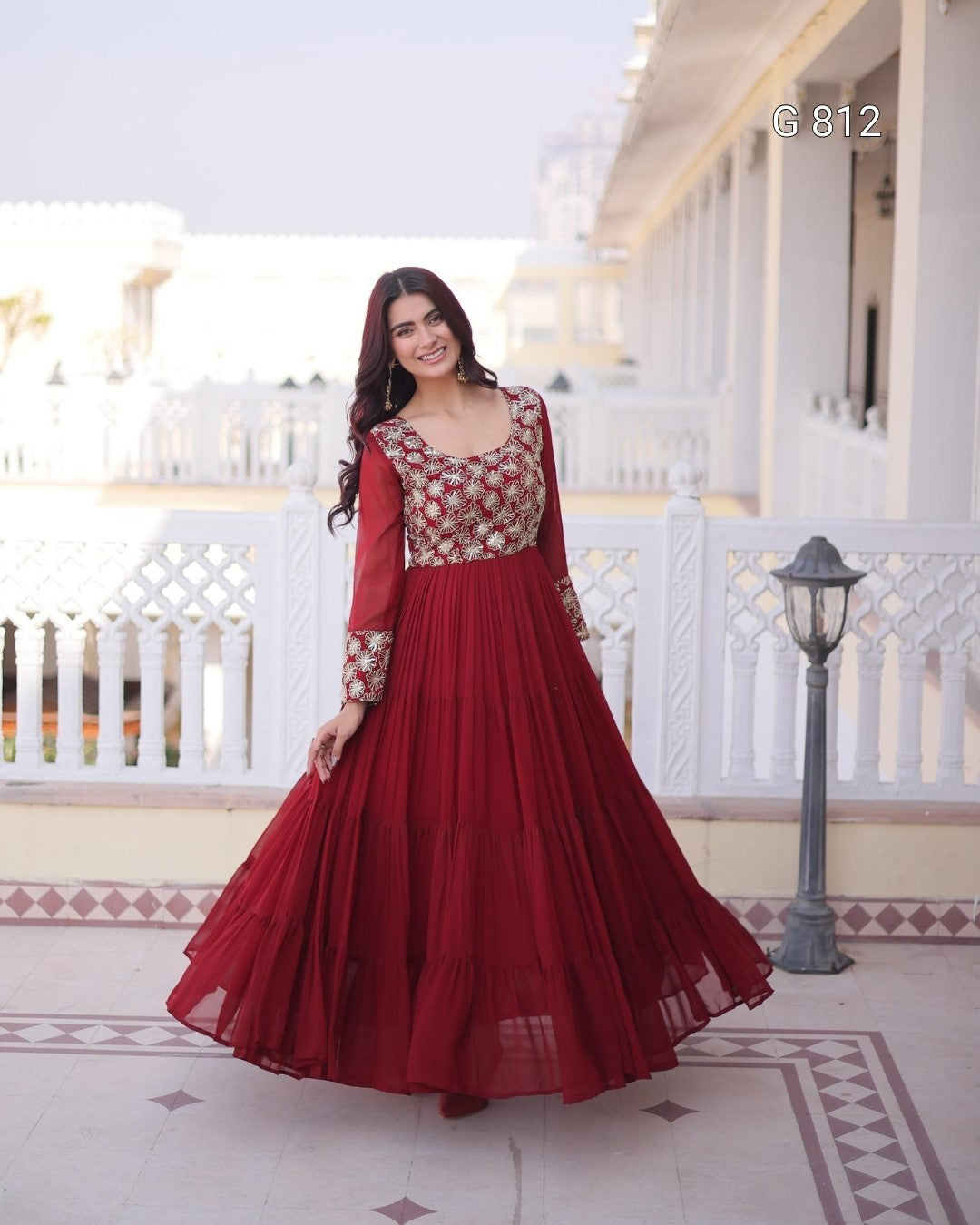 Woman in a red and gold traditional outfit standing on a balcony.