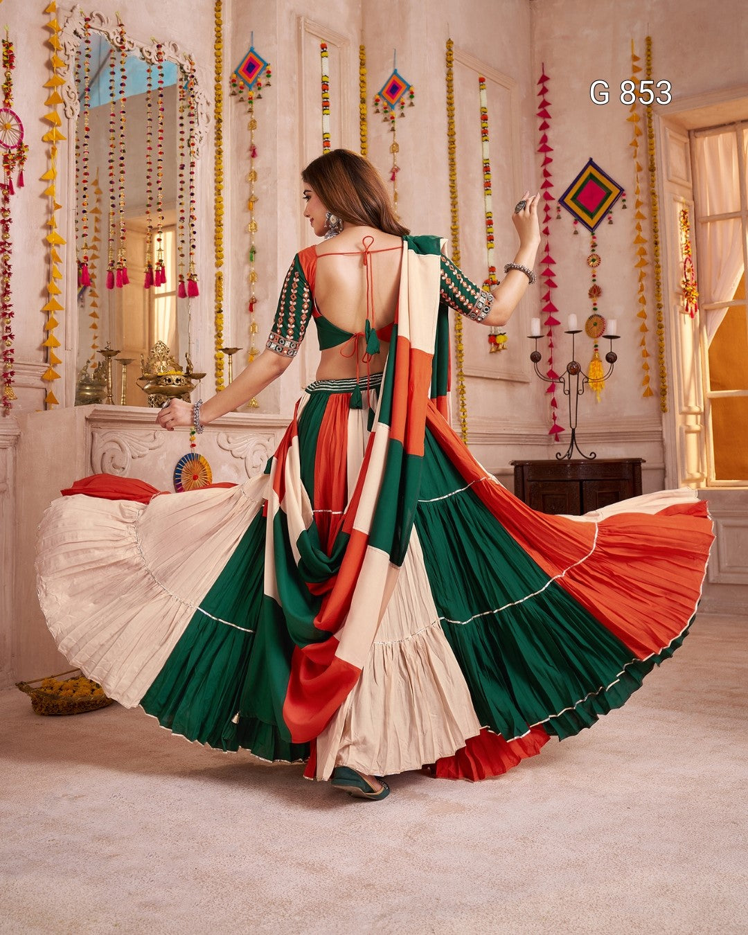 Woman in a colorful saree with a backless design, standing in a decorated room.