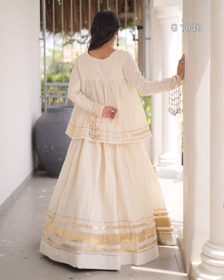 A woman wearing a cream-colored traditional Indian outfit with gold and silver zari embroidery, shown from the back in an outdoor corridor with white pillars.