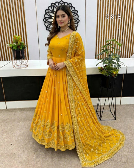 Woman wearing a yellow embroidered saree in an indoor setting with plants and decor.