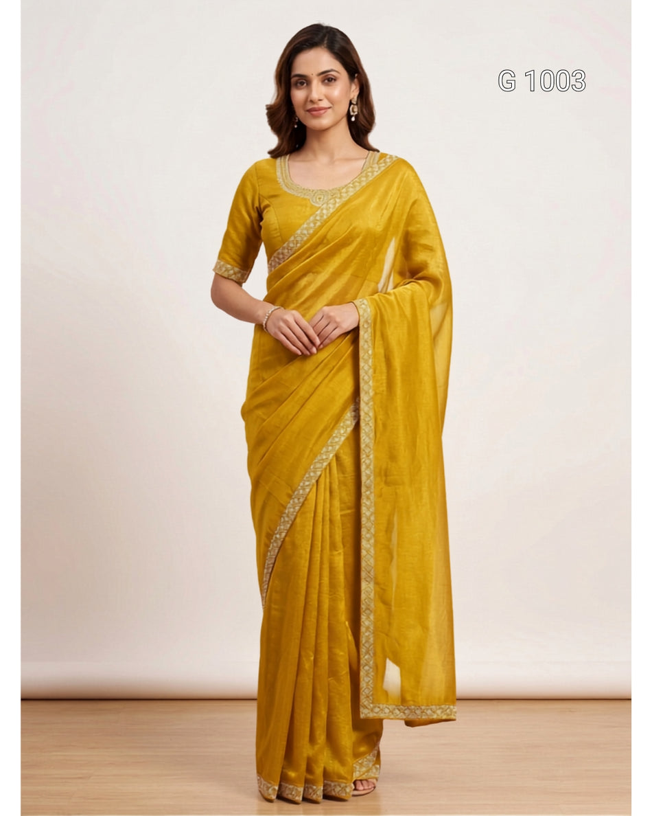A woman modeling a mustard yellow saree with gold embroidered borders, standing against a plain beige studio background. The text 'G 1003' appears in the top right corner.