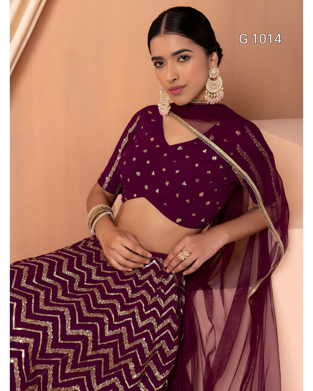 A woman models a deep purple georgette saree with gold zebra-patterned embroidery and a matching embroidered blouse. The image has a warm beige background and includes the text 'G 1014' in the top right corner.