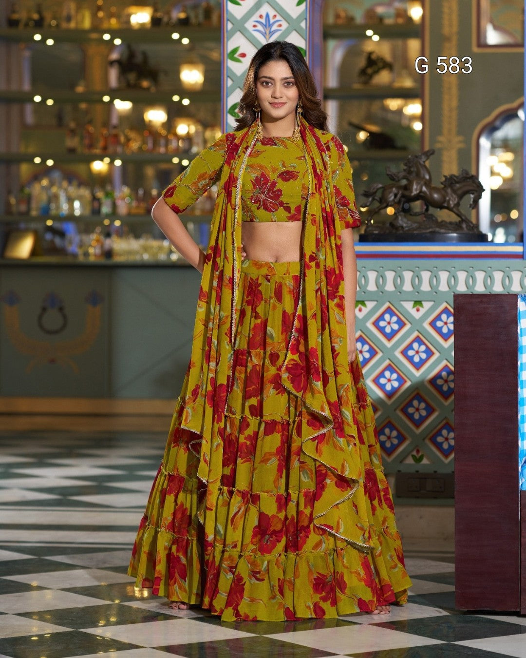 A woman models a traditional Indian lehenga choli set with a matching dupatta. The outfit features a vibrant yellow base with a bold red and orange floral print.