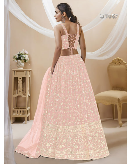 A woman modeling a light pink traditional Indian lehenga choli with intricate gold embroidery, shown from the back in a decorated indoor setting with draped white fabric.