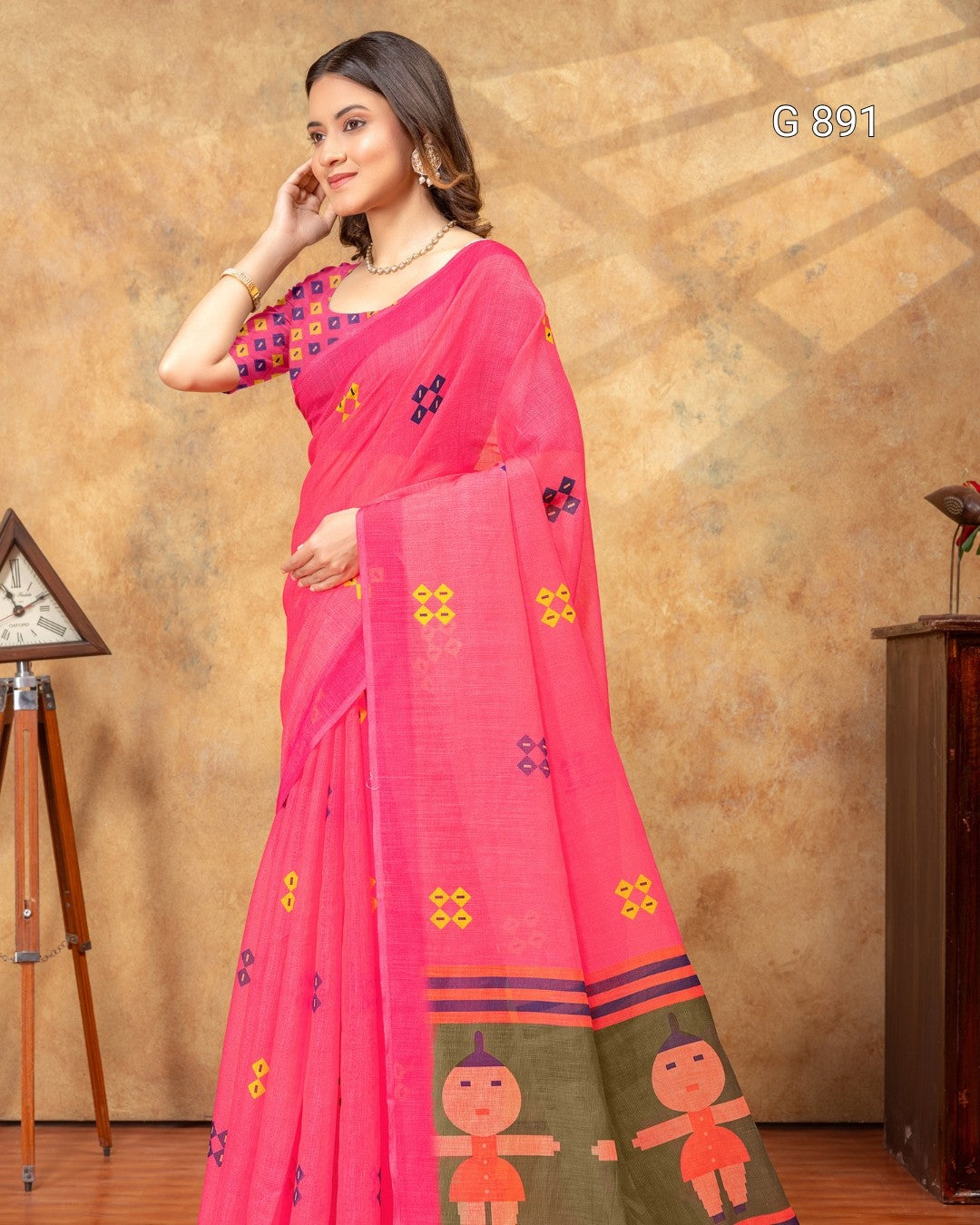 Woman wearing a pink saree with floral patterns against a beige wall.