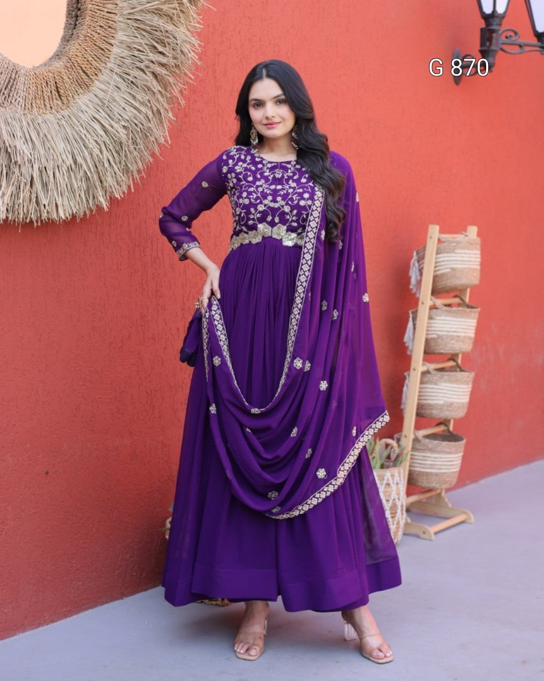 Woman in a purple traditional outfit with silver details against a red wall.