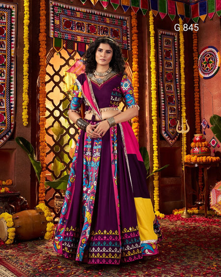 Woman in a colorful traditional outfit standing in front of decorative walls with patterns and flowers.