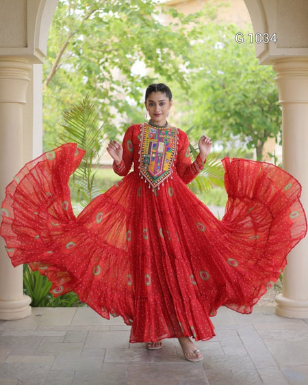 A woman wearing a vibrant red traditional long dress with a heavily embroidered multicolor neckline, captured mid-twist with her skirt flaring out. The setting is a stone walkway framed by columns with a lush green garden background.