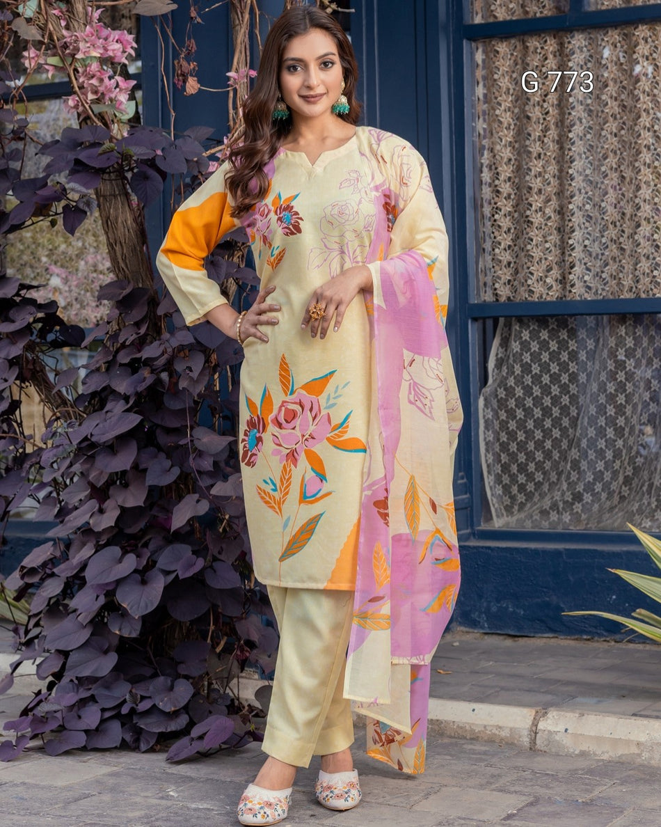 Woman in a light-colored traditional outfit with floral patterns standing in front of a decorative background.