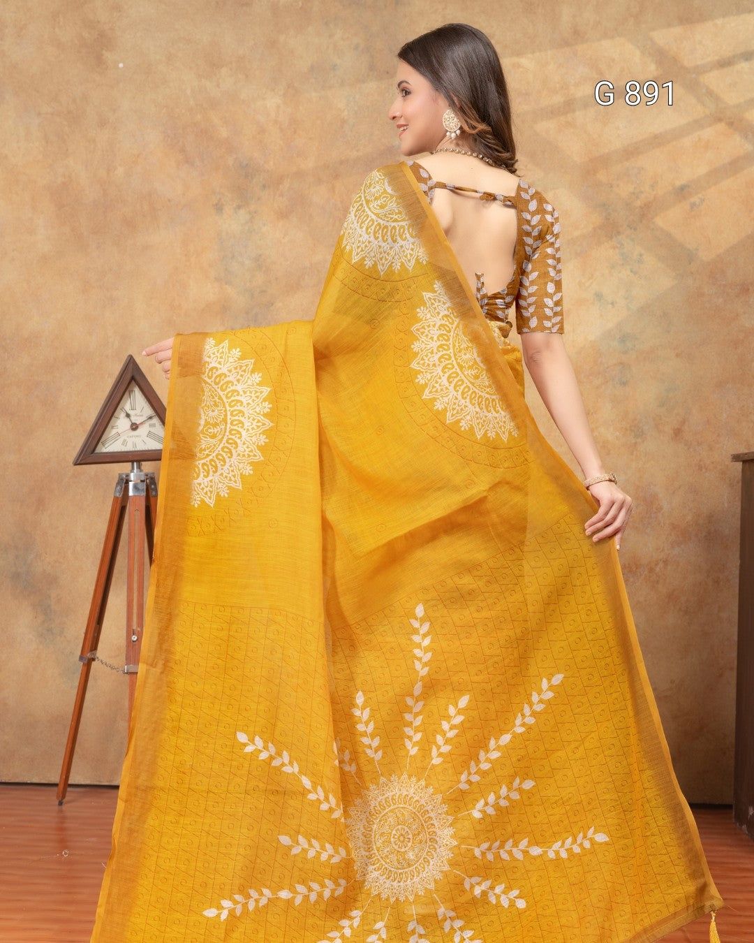 Woman wearing a yellow saree with white patterns against a brown background