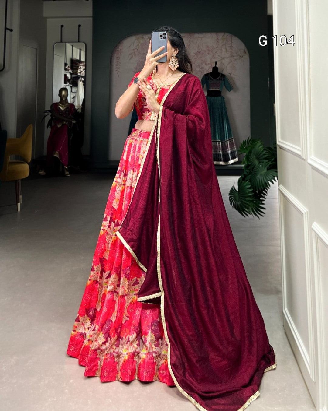 Woman taking a mirror selfie wearing a red and gold saree in a room.