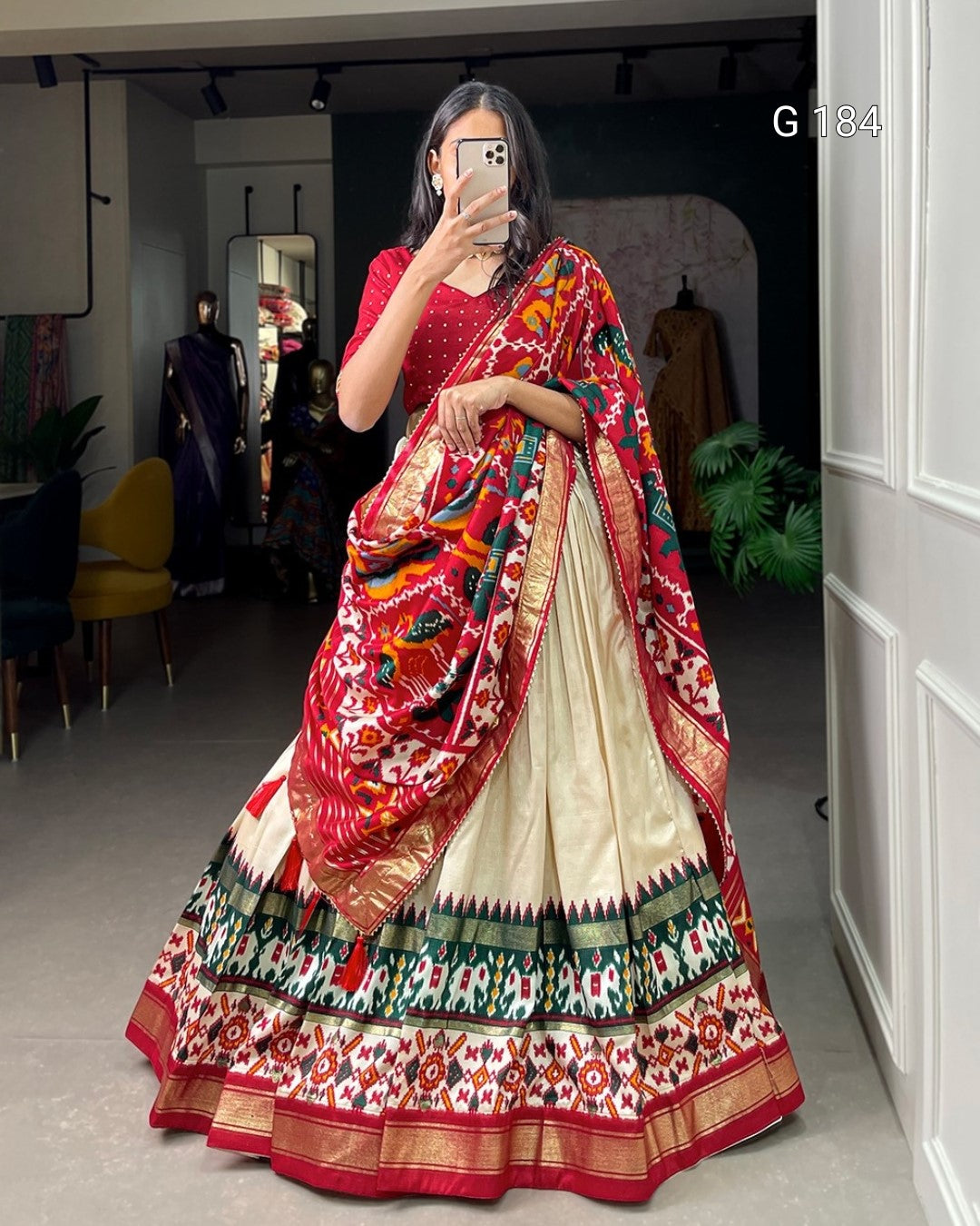 Woman wearing a colorful saree taking a mirror selfie in a room.