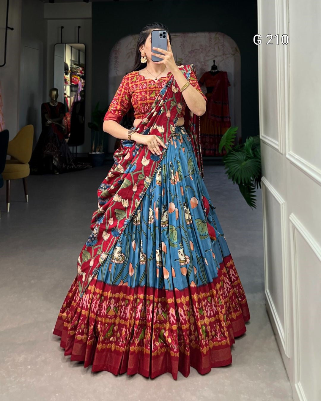 Woman wearing a colorful saree taking a mirror selfie in a room.