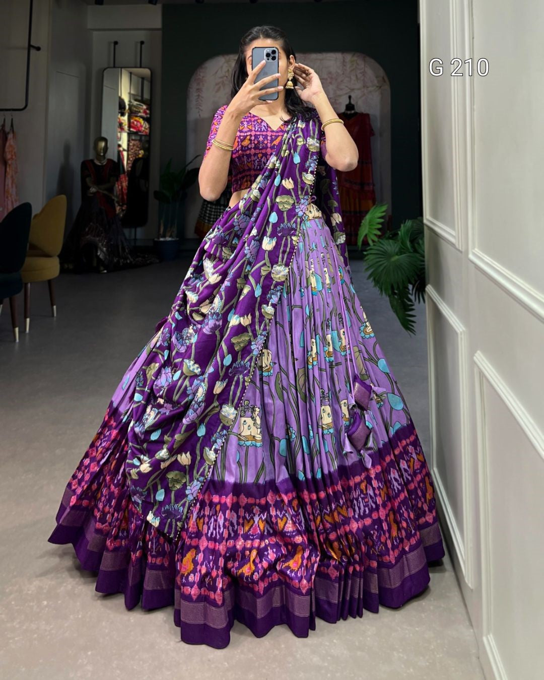 Person wearing a long, patterned purple dress in a room with a mirror.