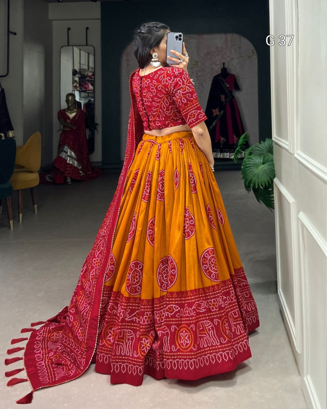 Woman taking a mirror selfie wearing a red and orange traditional outfit with intricate patterns.
