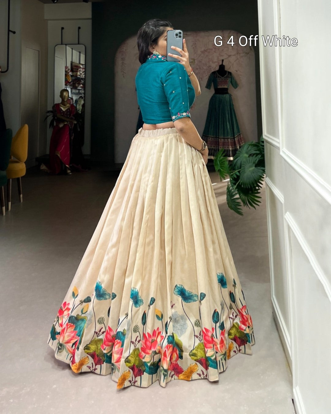 Woman taking a mirror selfie wearing a blue top and beige skirt with floral designs.