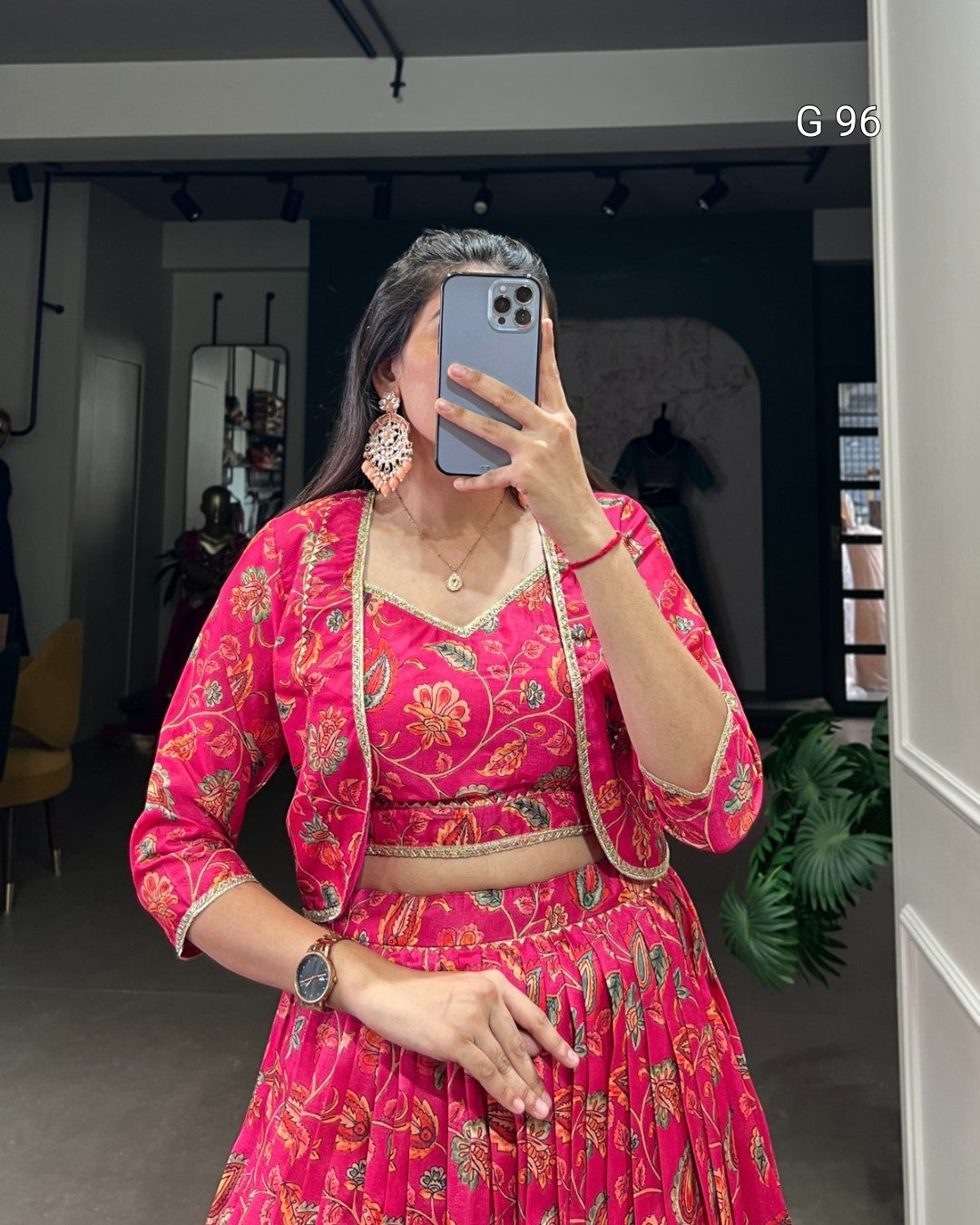 Person wearing a bright pink traditional outfit with floral patterns, taking a mirror selfie.