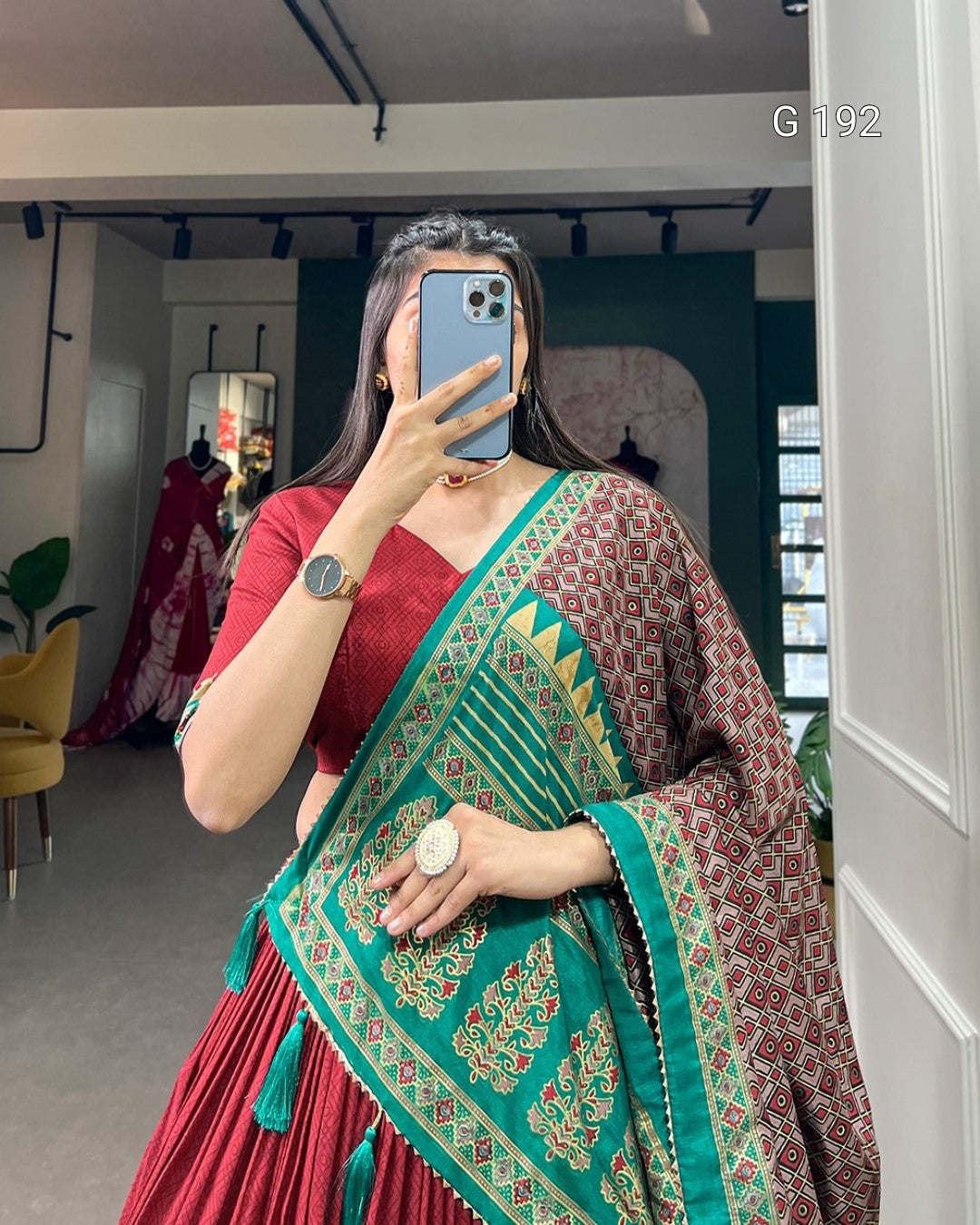 Person wearing a red and green patterned saree taking a mirror selfie.