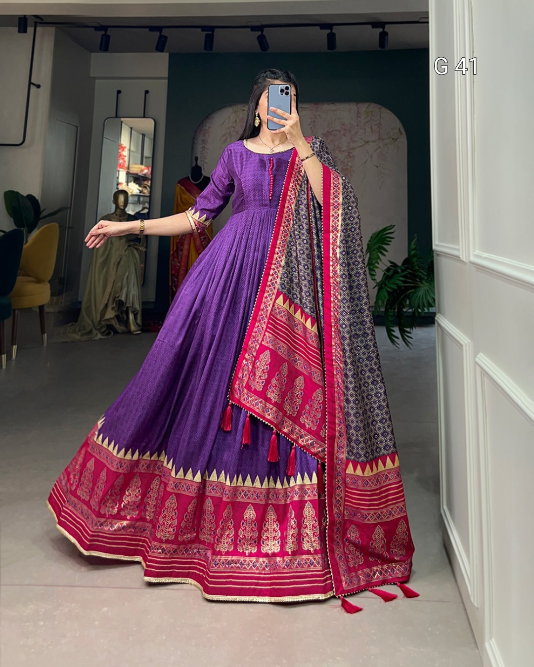 Person wearing a traditional outfit with a purple and pink design, standing in a room.