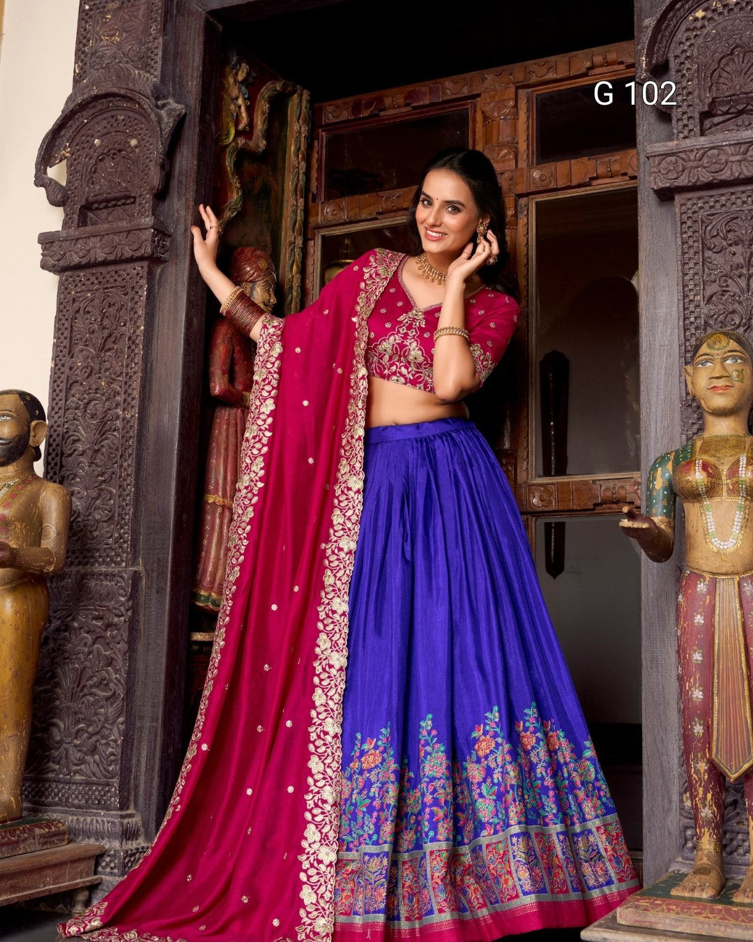 Woman in a traditional blue and pink saree standing in front of decorative wooden doors.