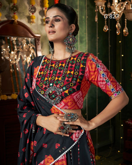 Woman wearing a traditional colorful saree with intricate patterns and jewelry in a decorative setting.