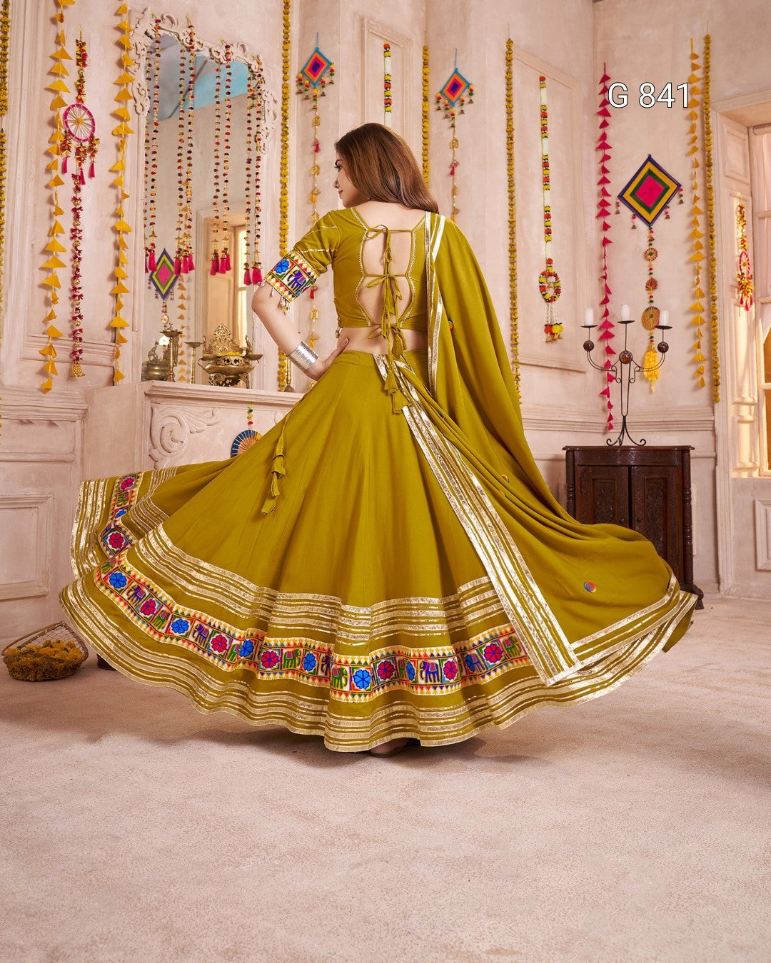 Woman in a green traditional outfit with colorful embroidery in a decorated room.