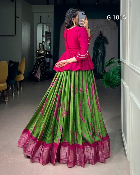 A woman takes a mirror selfie in a boutique wearing a traditional Indian outfit consisting of a bright pink peplum top and a voluminous green skirt with pink and gold zari patterns and borders. The text 'G 1015' is visible in the top right corner.