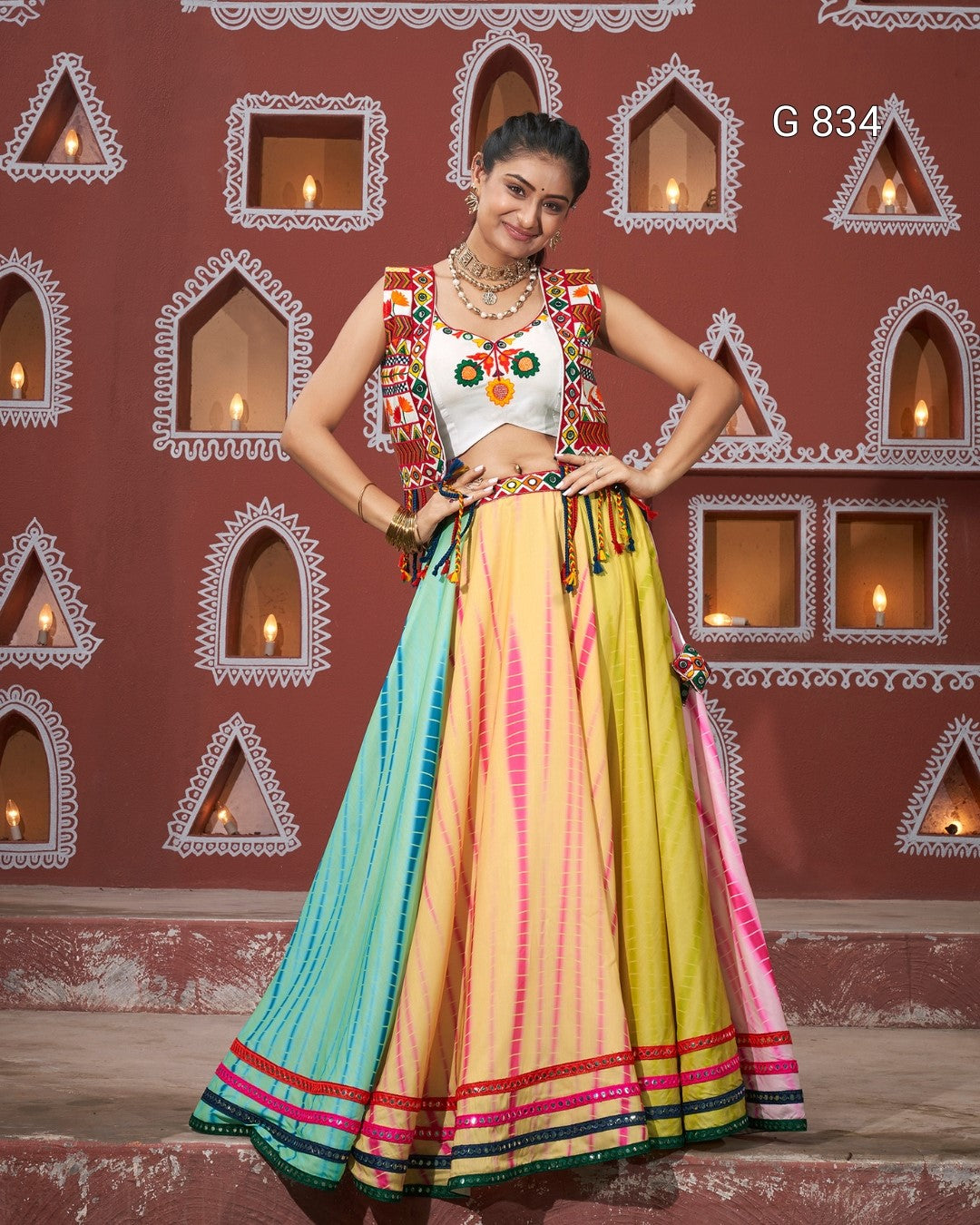 Woman in a colorful traditional outfit standing against a decorative wall.