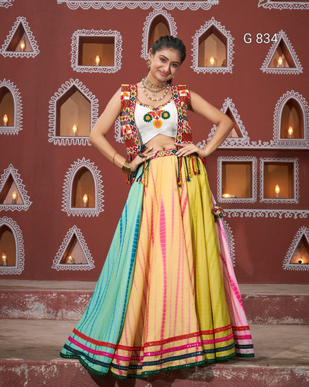 Woman in a colorful traditional outfit standing against a decorative wall.