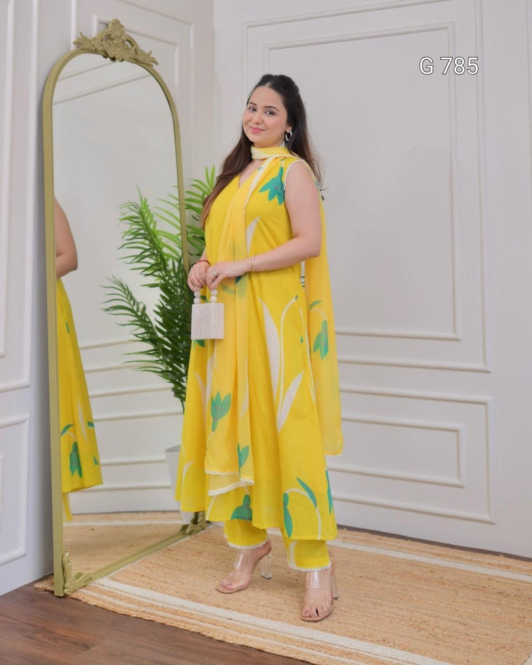 Woman in a yellow outfit with green patterns standing in front of a mirror.