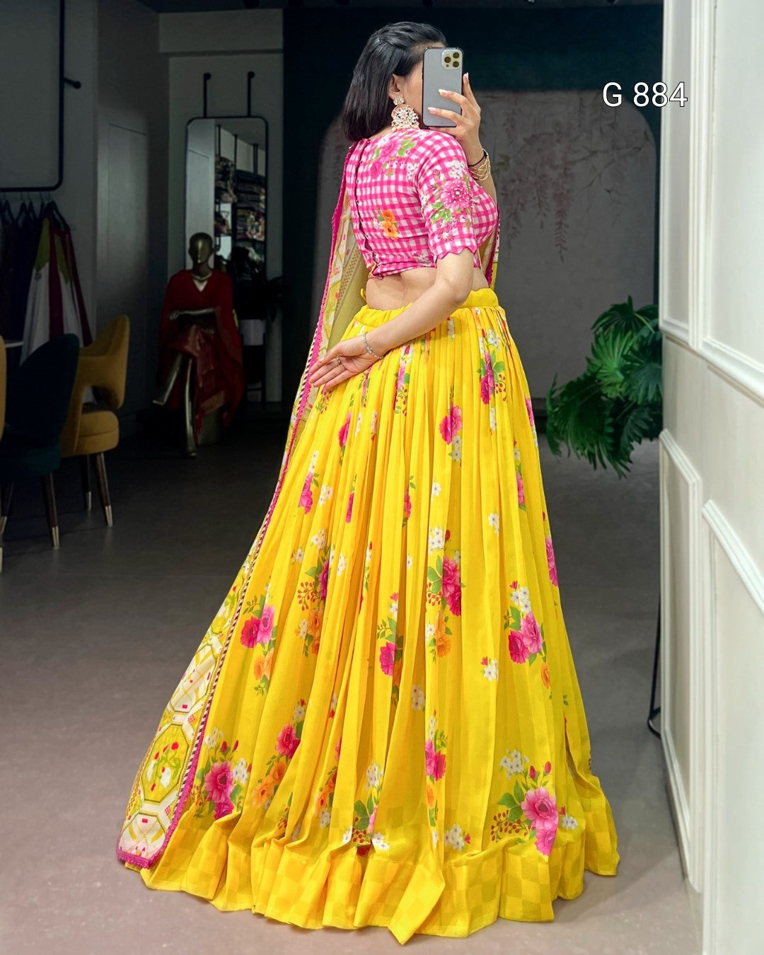 Woman in a yellow floral saree with a pink blouse taking a mirror selfie.