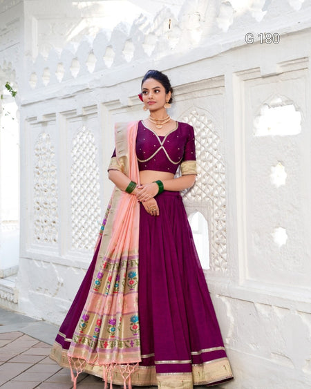 Woman in a purple traditional outfit with a pink dupatta against a white decorative wall.