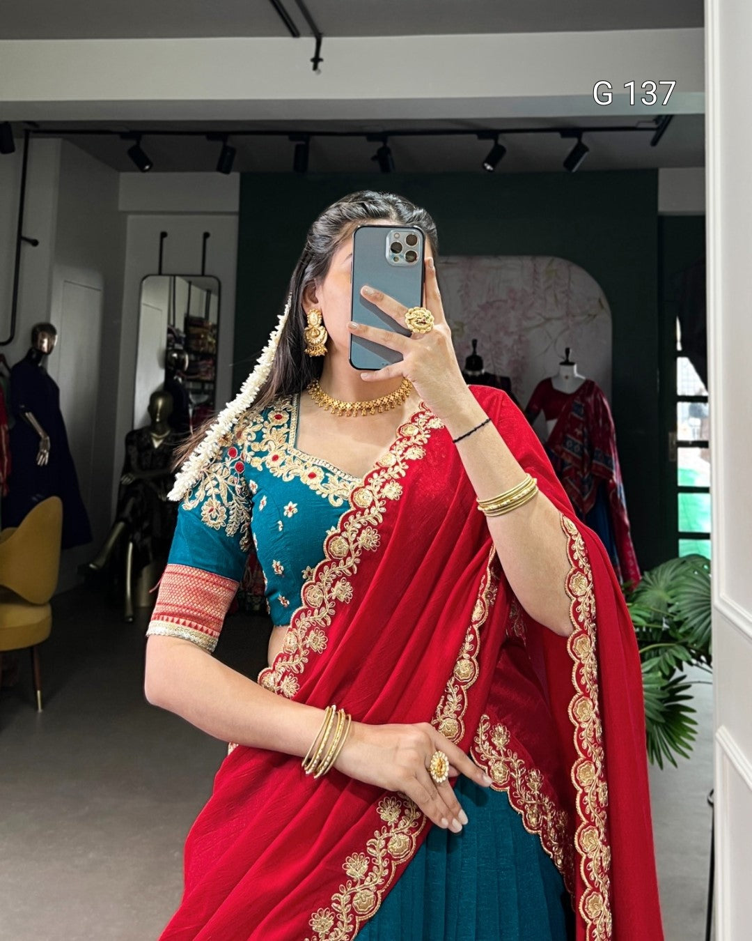 Woman in a traditional outfit with a red and blue saree, taking a mirror selfie.