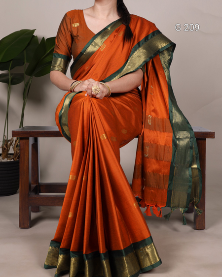 Orange saree with green border worn by a person, sitting on a wooden stool.