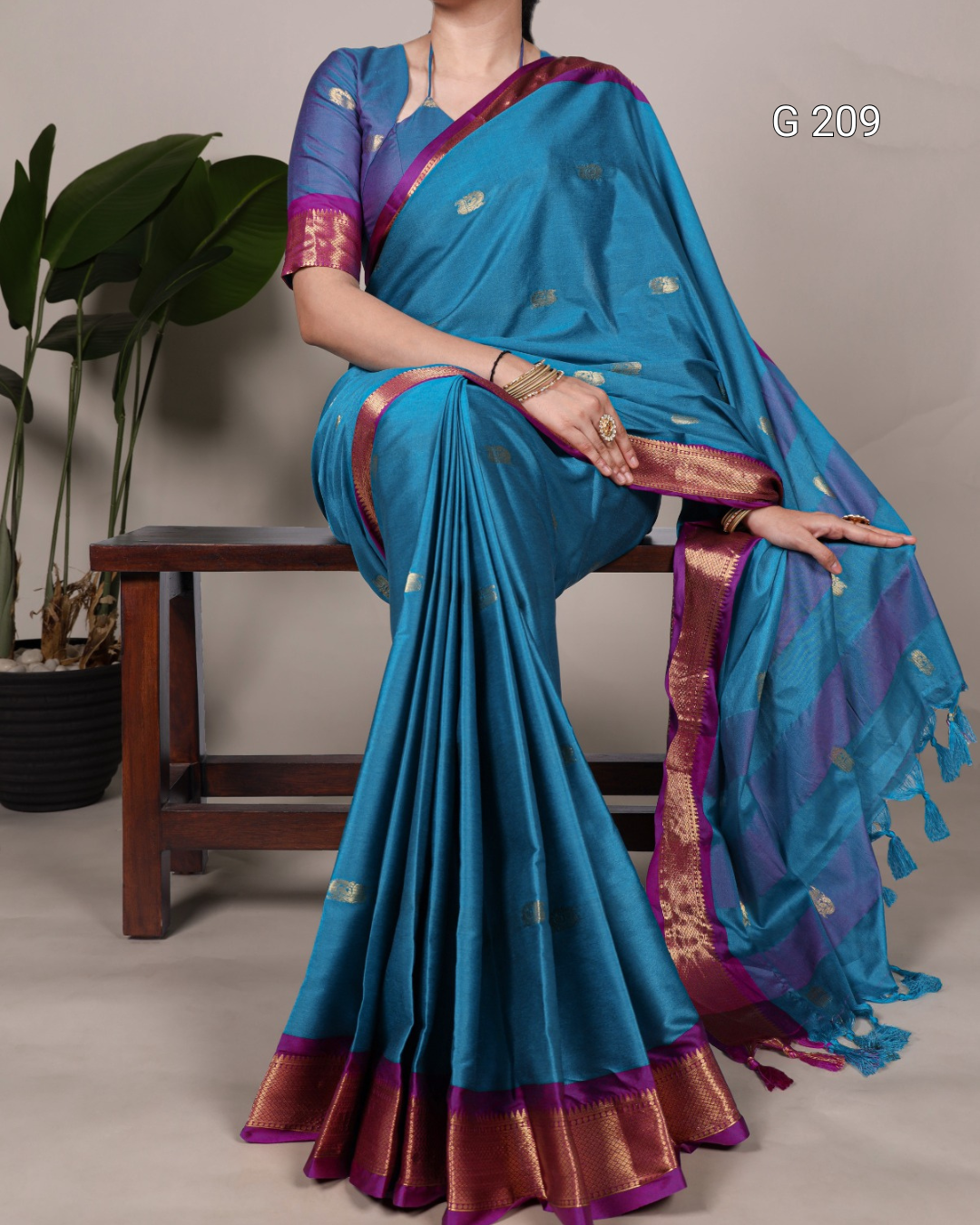 Woman wearing a blue saree with a purple border, sitting on a wooden bench.