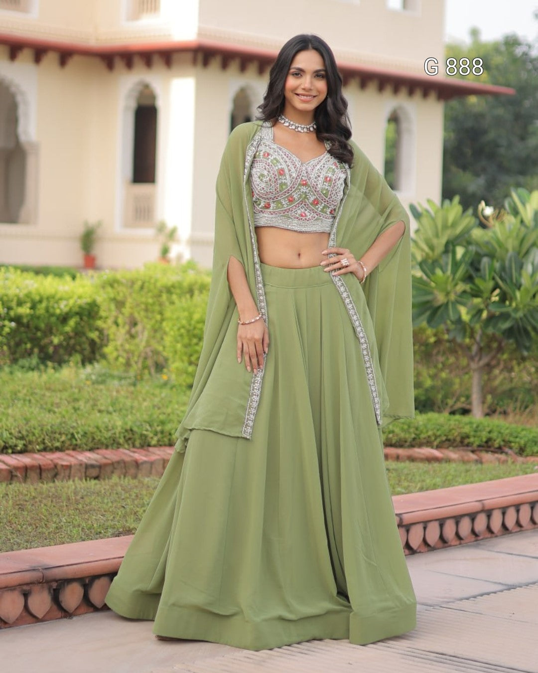Woman in a green traditional outfit standing outdoors with a building and garden in the background