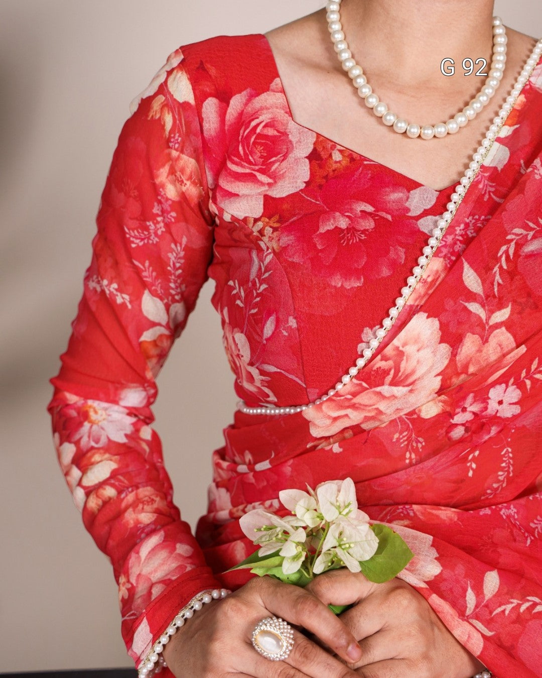 Red floral saree with a pearl border and a corsage on a neutral background