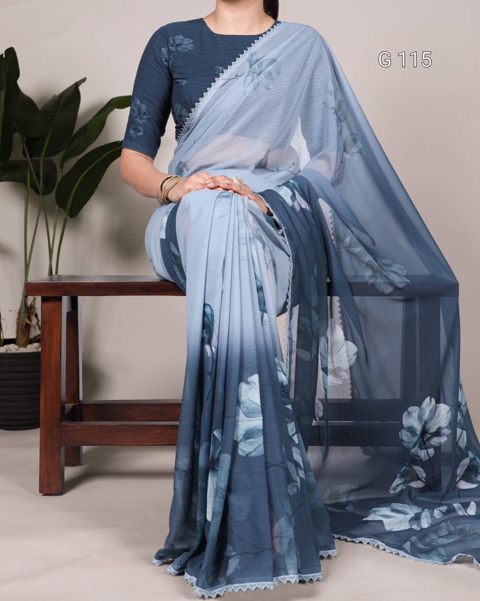 Woman wearing a blue saree with a floral pattern, sitting on a chair against a neutral background.