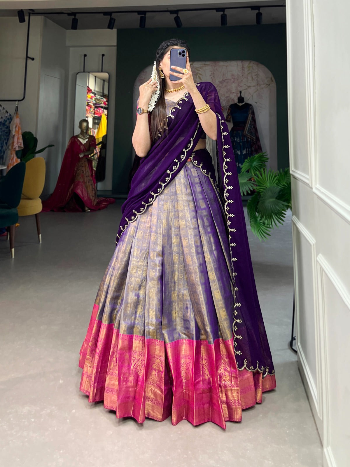 Person wearing a purple and pink saree in a room with mirrors and clothing in the background.