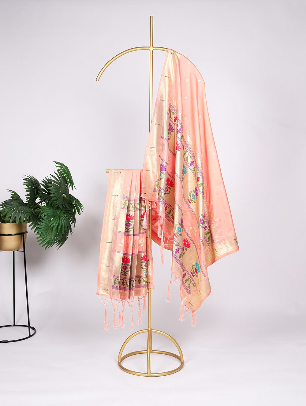 Peach-colored scarf with floral patterns draped over a gold stand against a white background.