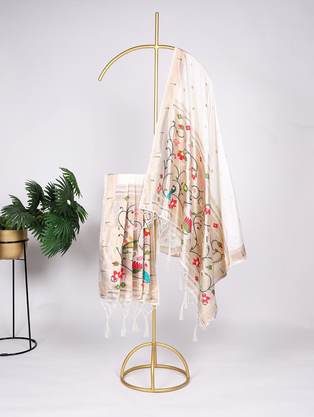 Decorative scarf with floral patterns hanging on a gold stand against a white background