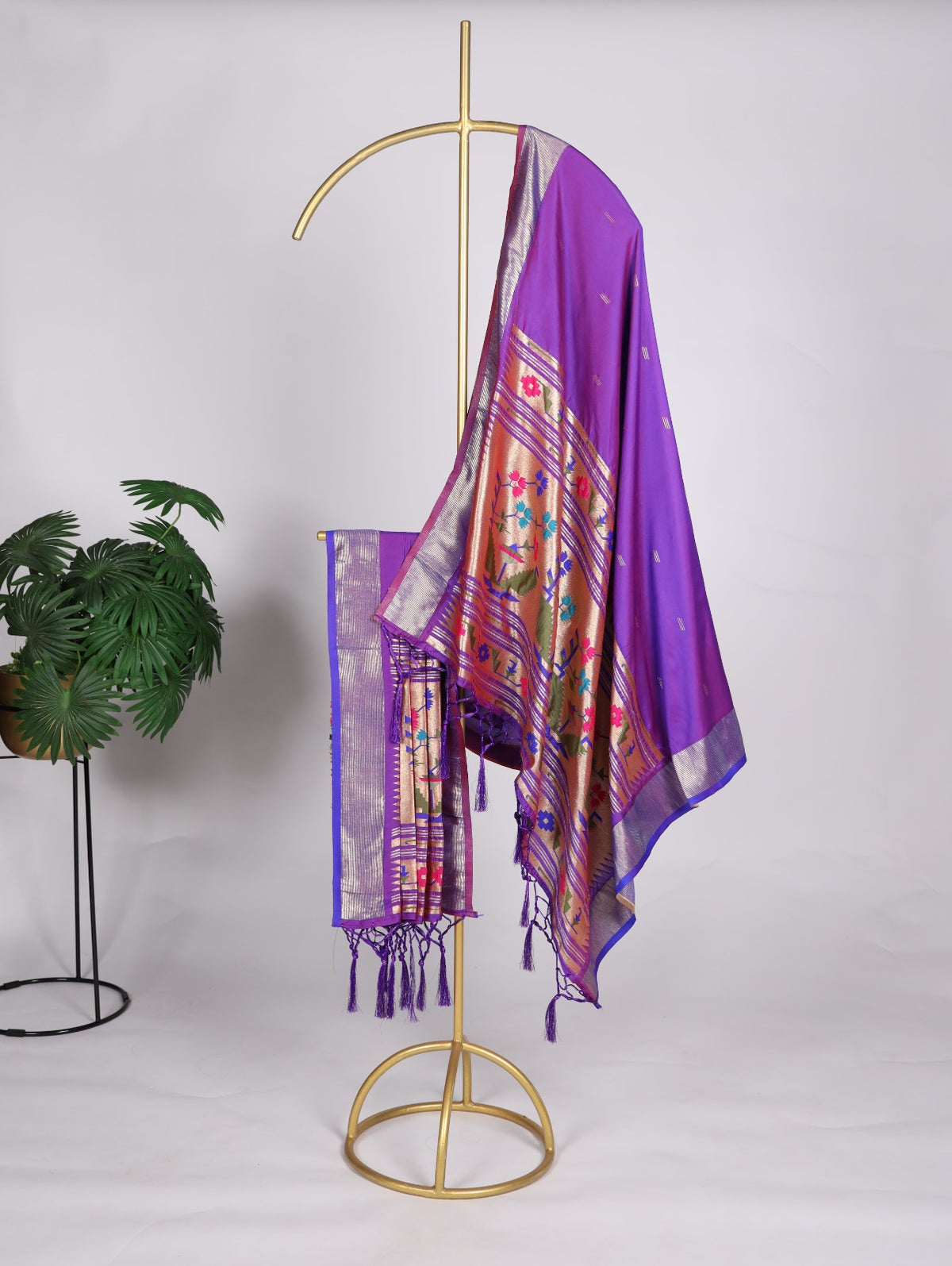 Purple scarf with floral patterns hanging on a gold stand against a white background