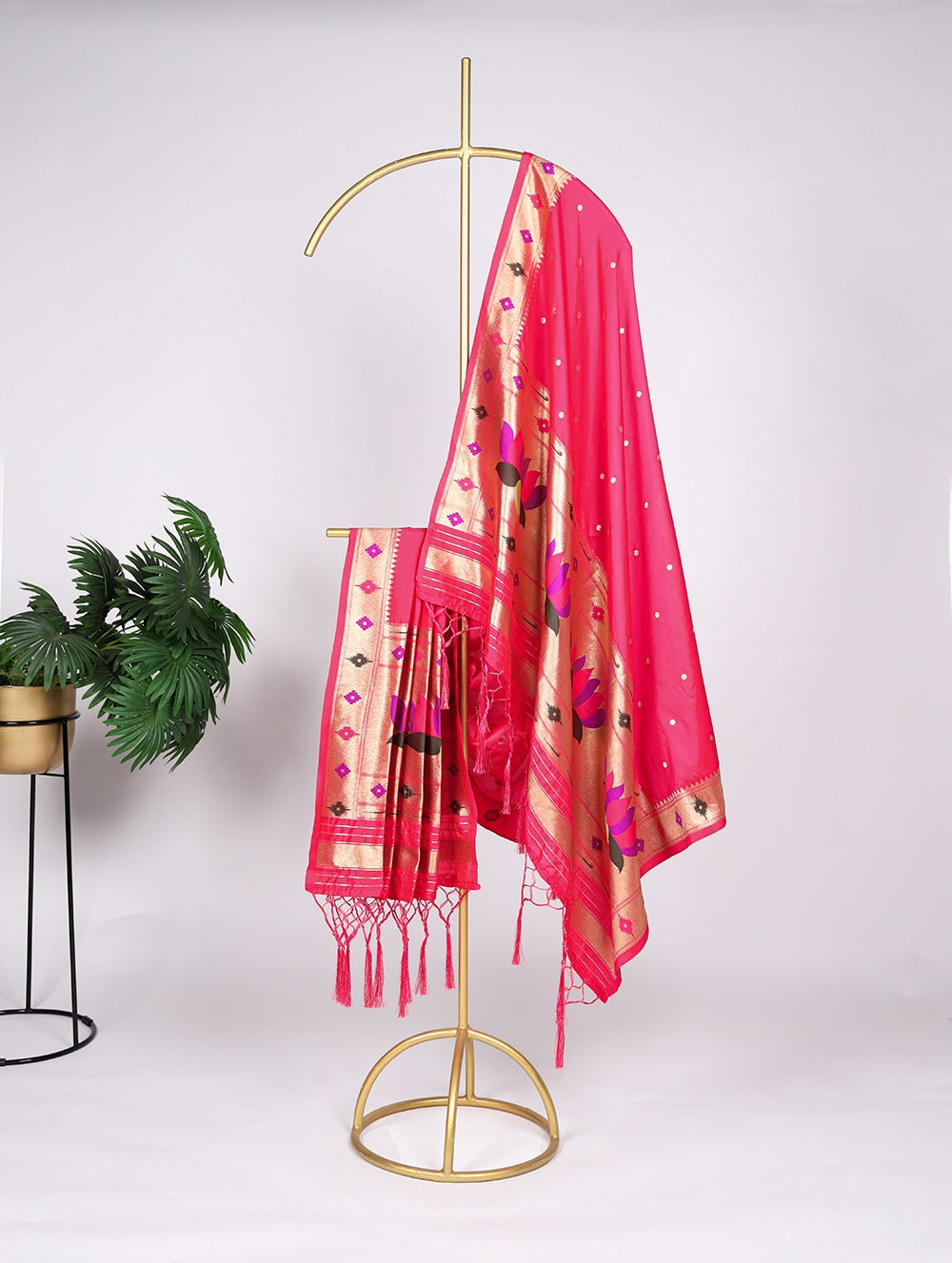 Pink saree with gold border draped over a gold stand against a white background