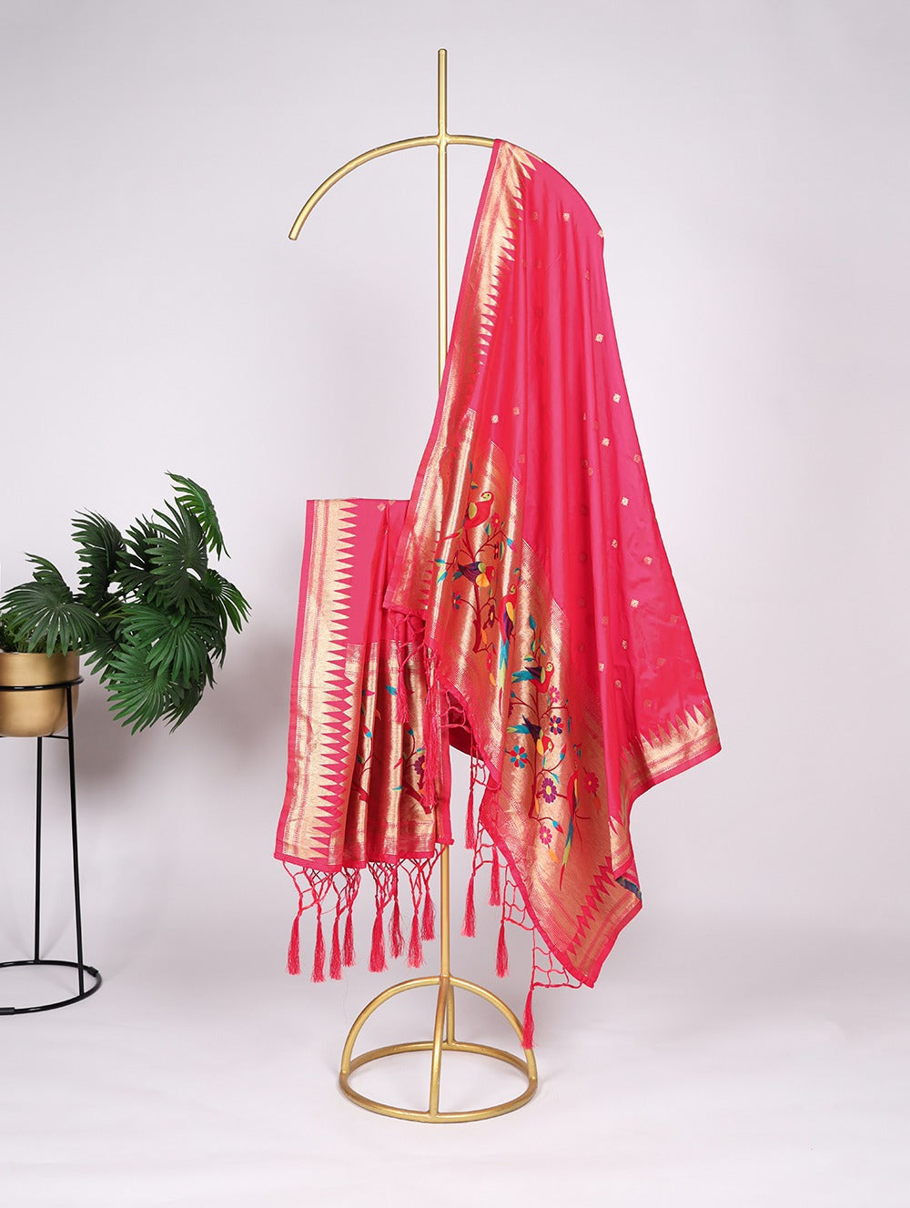 Pink saree with a gold border on a gold stand against a white background