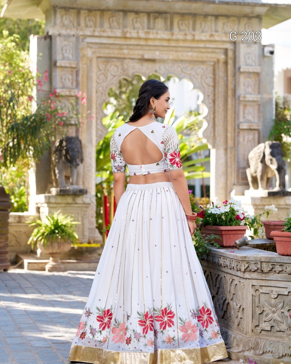 Woman in a white traditional outfit with floral patterns standing in an outdoor setting.