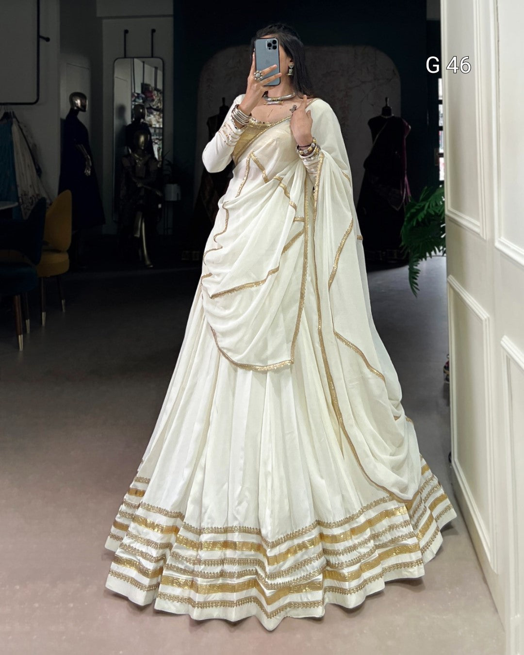 Person wearing a white saree with gold accents in an indoor setting.
