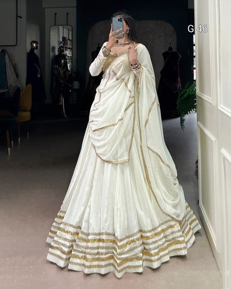 Person wearing a white saree with gold accents in an indoor setting.