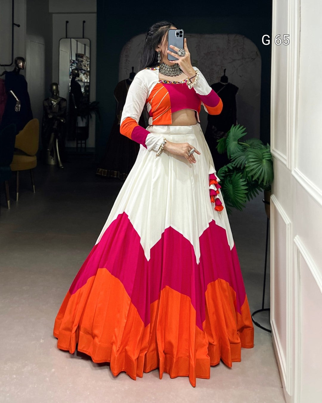 Woman taking a mirror selfie wearing a colorful traditional outfit with an orange, white, and pink design.