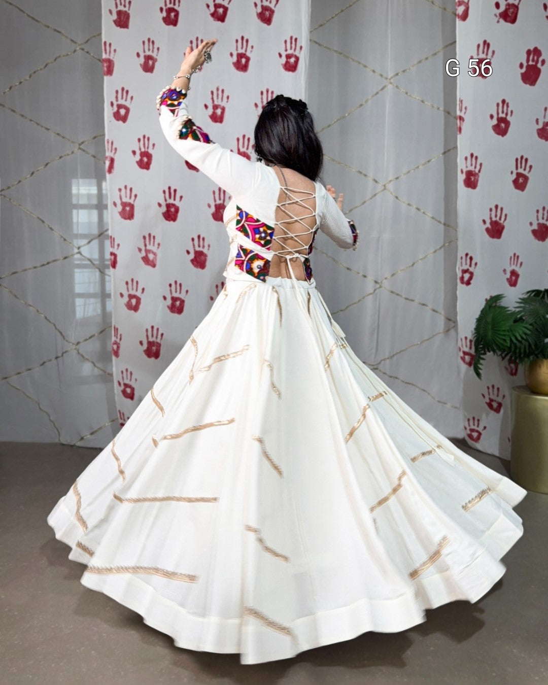 Woman in a white dress with gold patterns dancing in front of a curtain with red handprints.